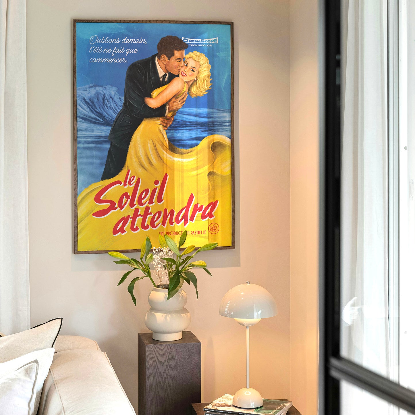 Affiche rétro style années 40 montrant un couple enlacé sur fond bleu. La femme porte une monumentale robe jaune fluide évoquant une coulée d'or. Titre en rouge : "Le soleil attendra" accroché au mur avec une plante et une lampe dessous.