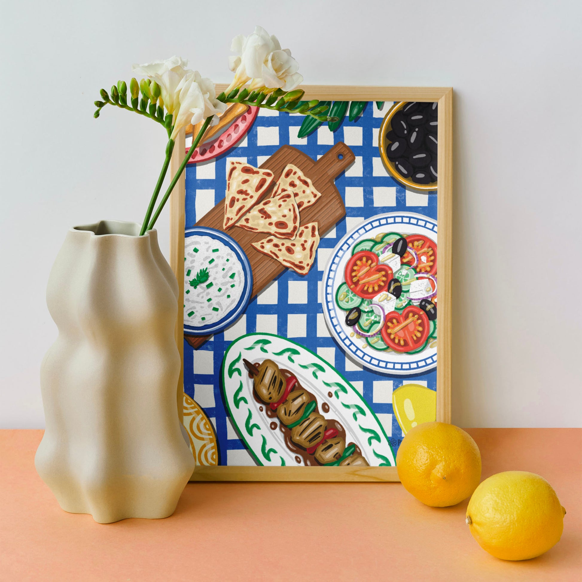 Affiche repas grec avec des plats typiques. Sur une table avec une nappe à carreaux bleu. Le tableau est posé sur un table avec un vase, des fleurs et des citrons.