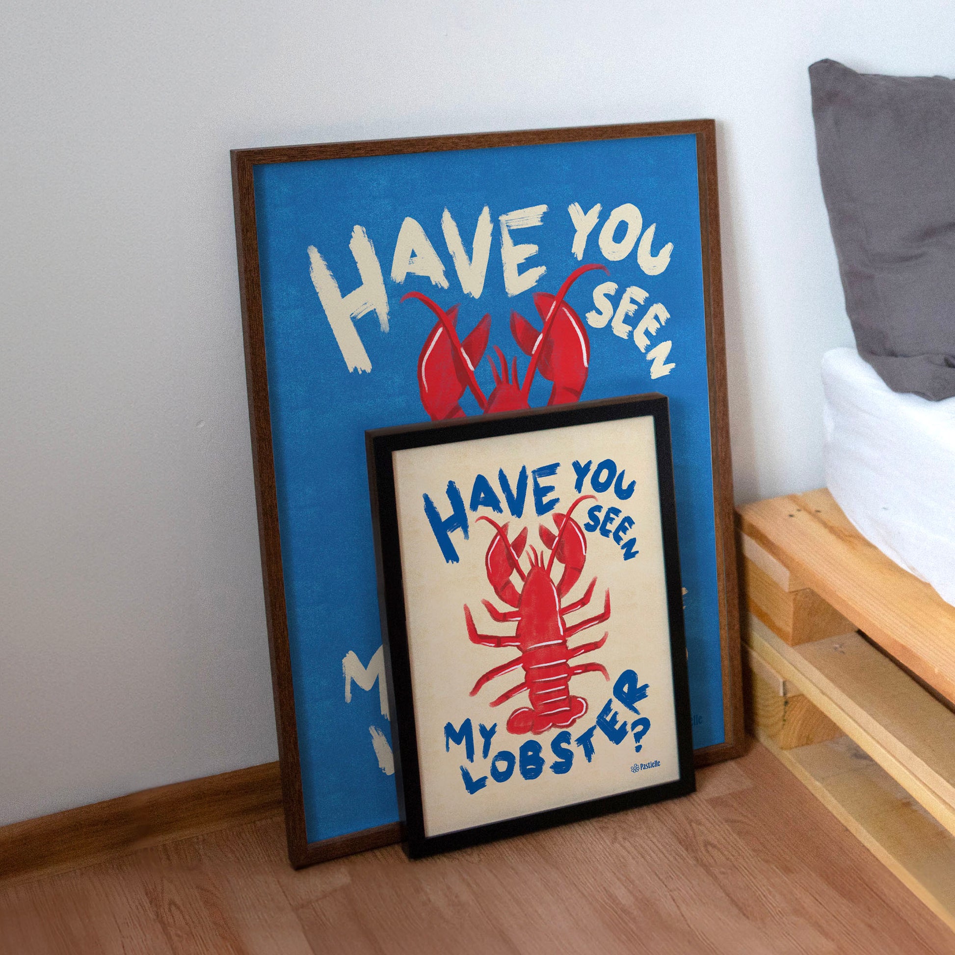 Deux affiches posées à côté d'un lit, elles représentent l'affiche du homard l'une est grande et placé derrière et l'autre et devant.