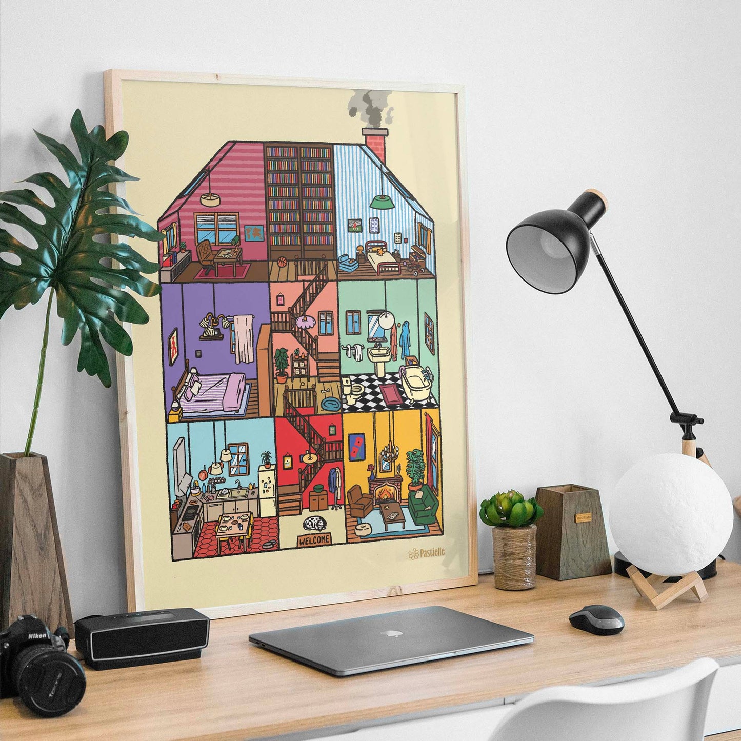 Affiche d’une maison ouverte avec 6 pièces, un peu comme une maison de poupée, posée sur un bureau avec différents objets.
