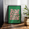 Affiche rise and shine écrit en rose sur fond vert dans un cadre, posée au sol avec une plante à côté