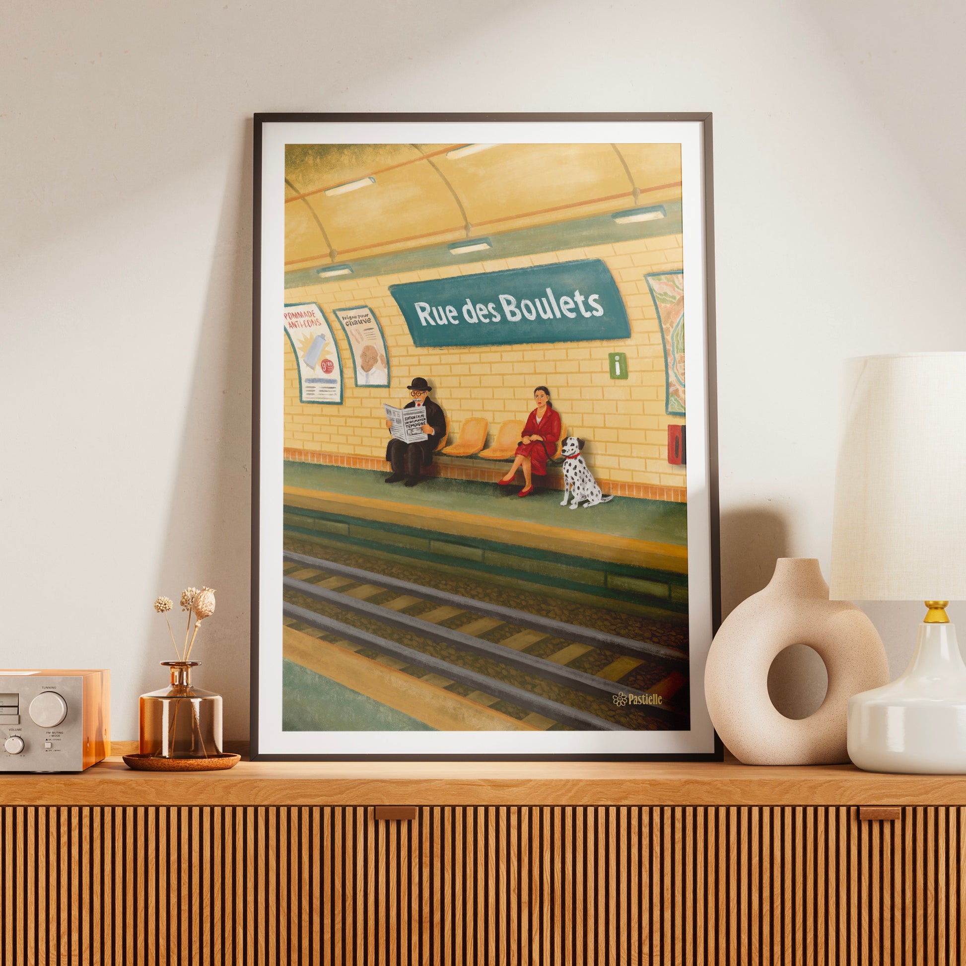 Affiche Pastielle Rue des Boulets – affiche rétro illustrée d’un quai de métro parisien avec un homme, une femme et un dalmatien, posée sur un meuble en bois