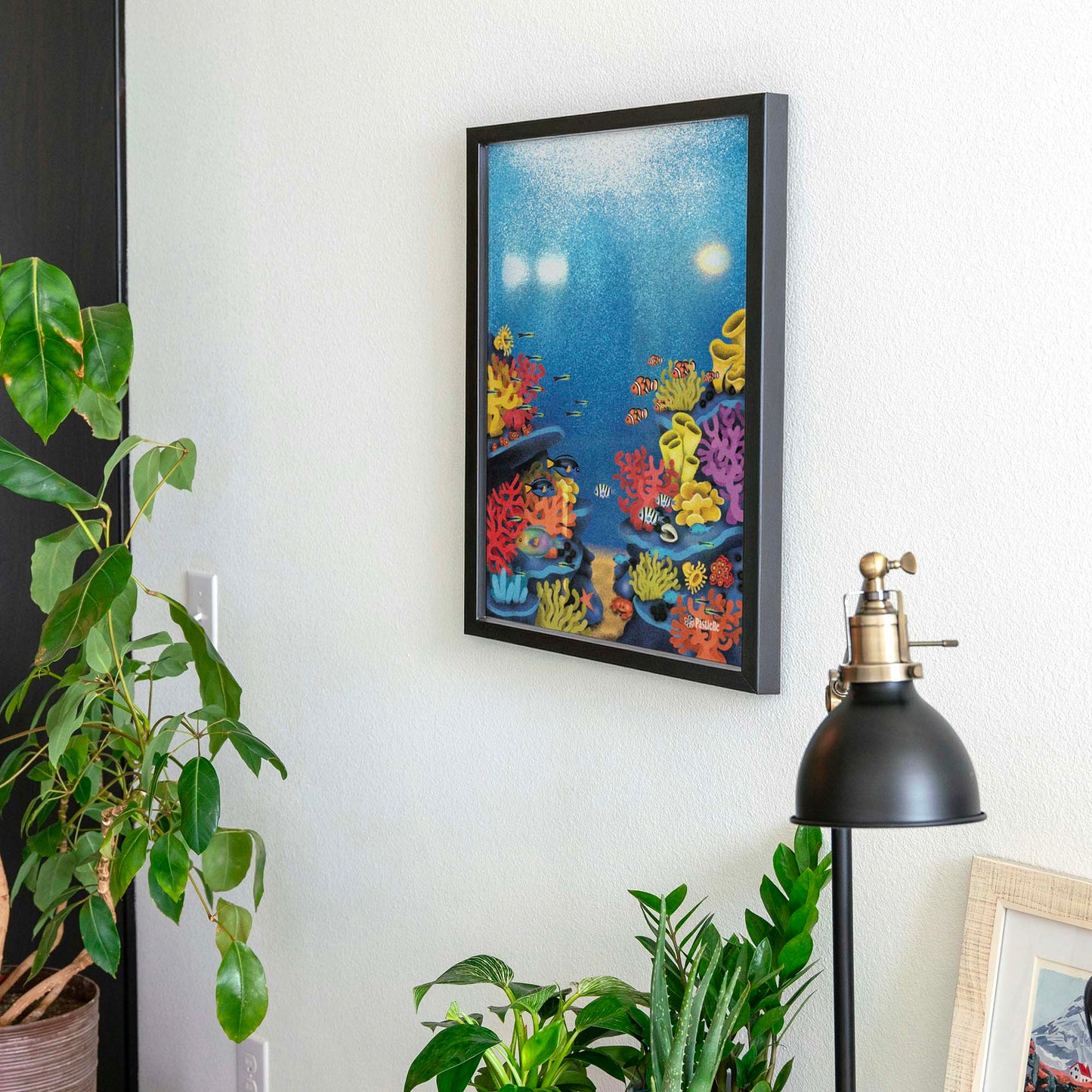 Affiche d'un récif avec des poissons dans un cadre accrochée au mur avec des plantes autour. 