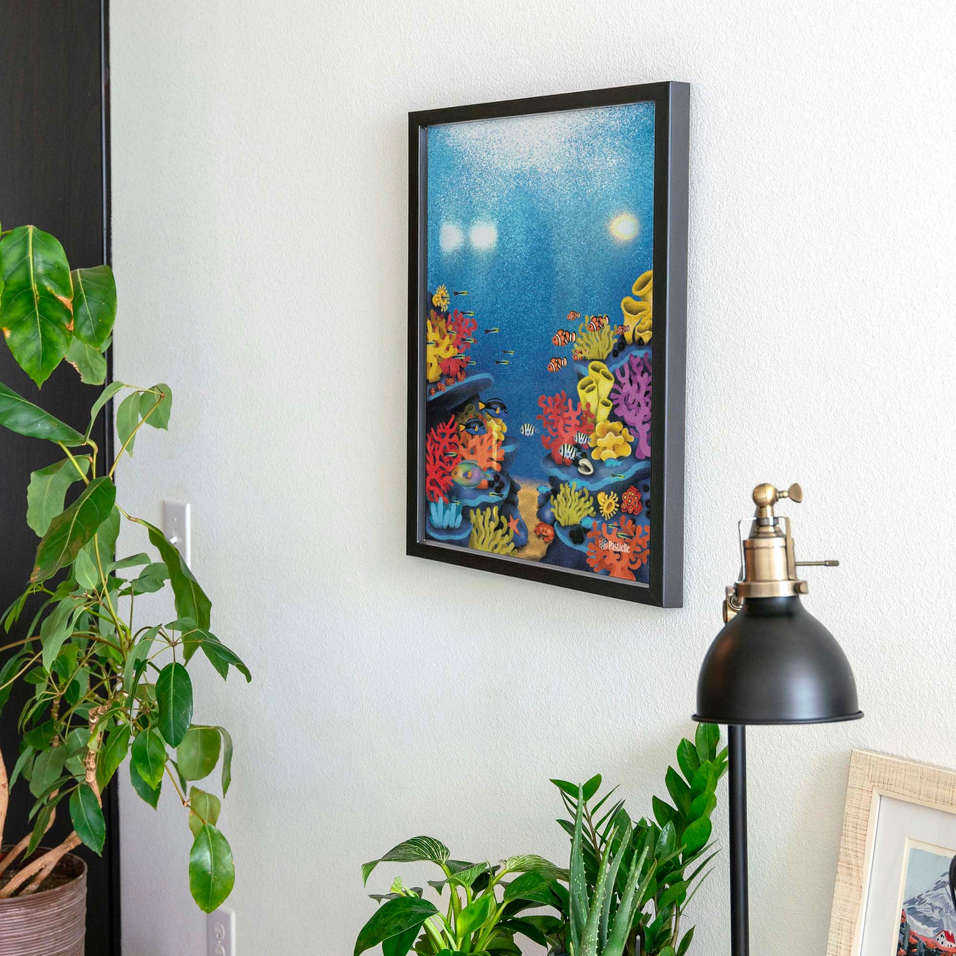 Affiche d'un récif avec des poissons dans un cadre accrochée au mur avec des plantes autour. 